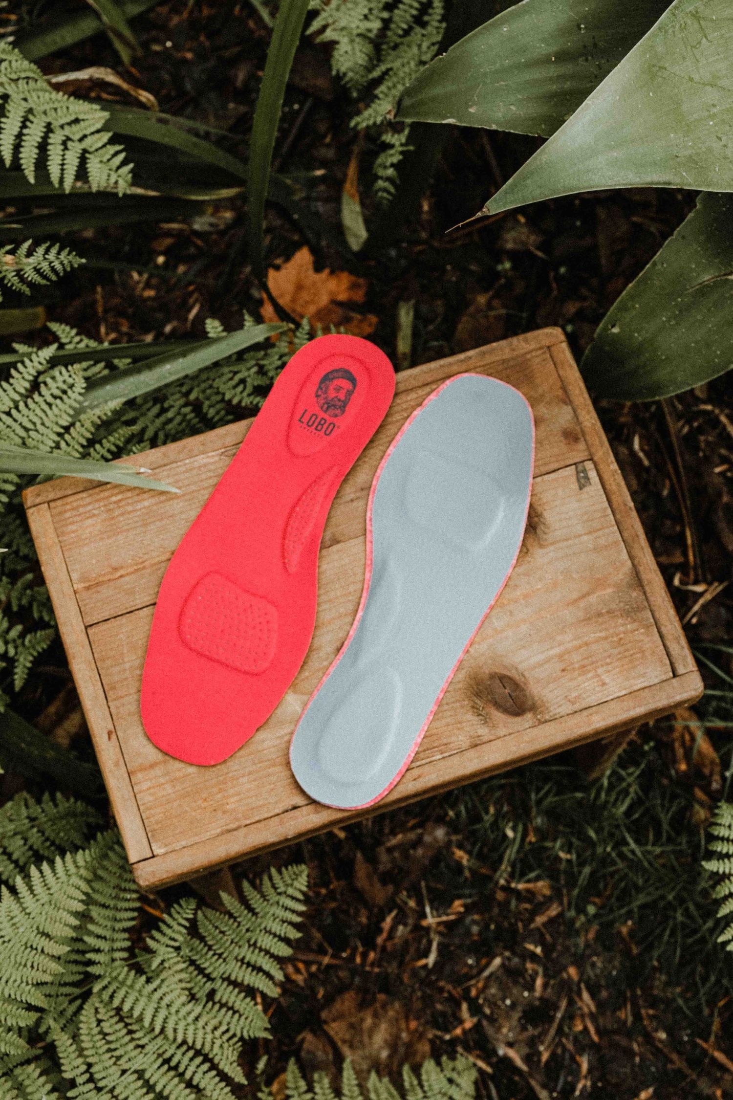 Pair of red Lobo Insoles leather insoles photographed from above on a wooden box in a natural setting.