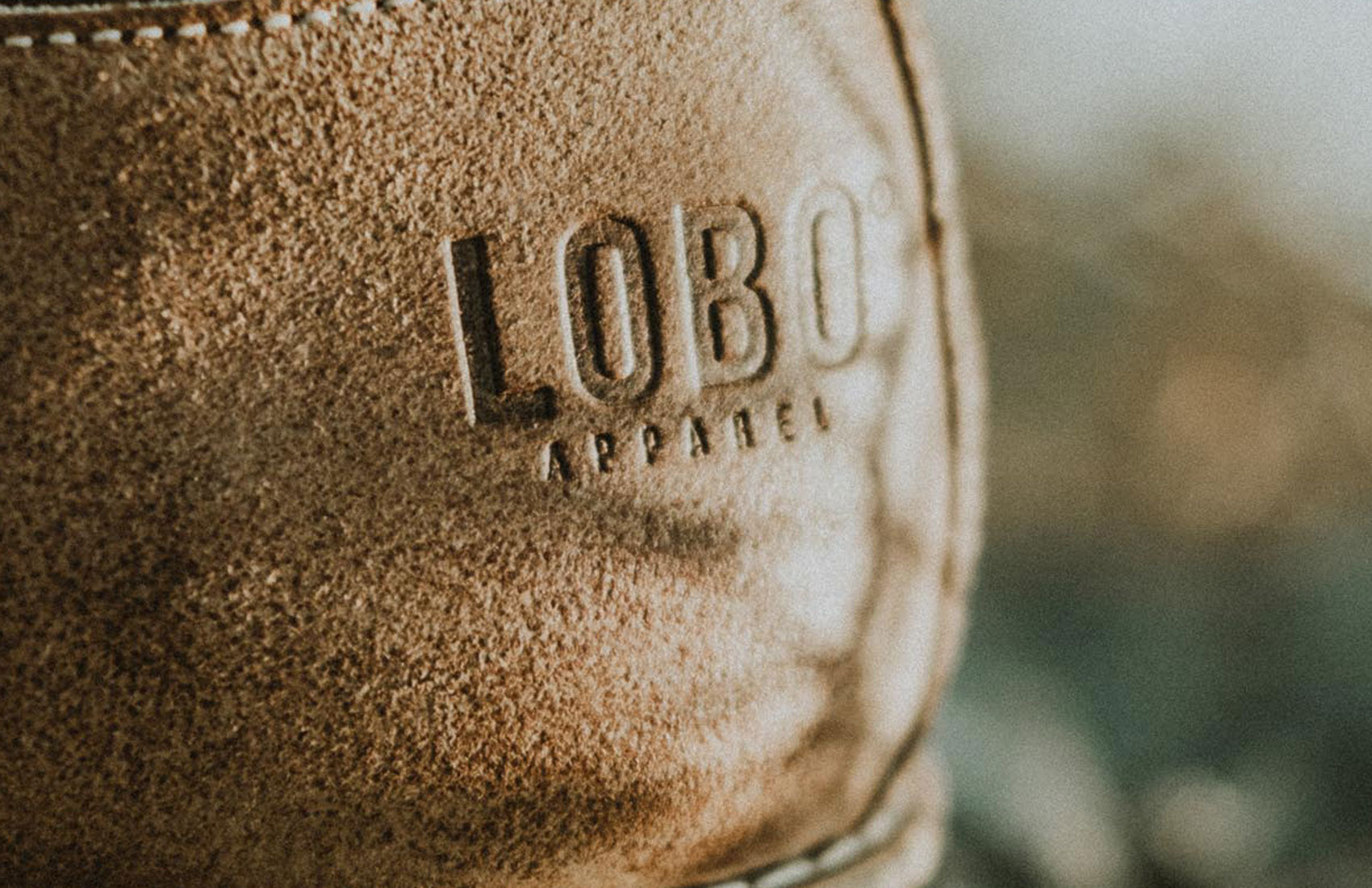 Close-up of the LOBO Apparel logo embossed on a brown suede leather texture. Detail of quality and artisanal craftsmanship of a brand product.
