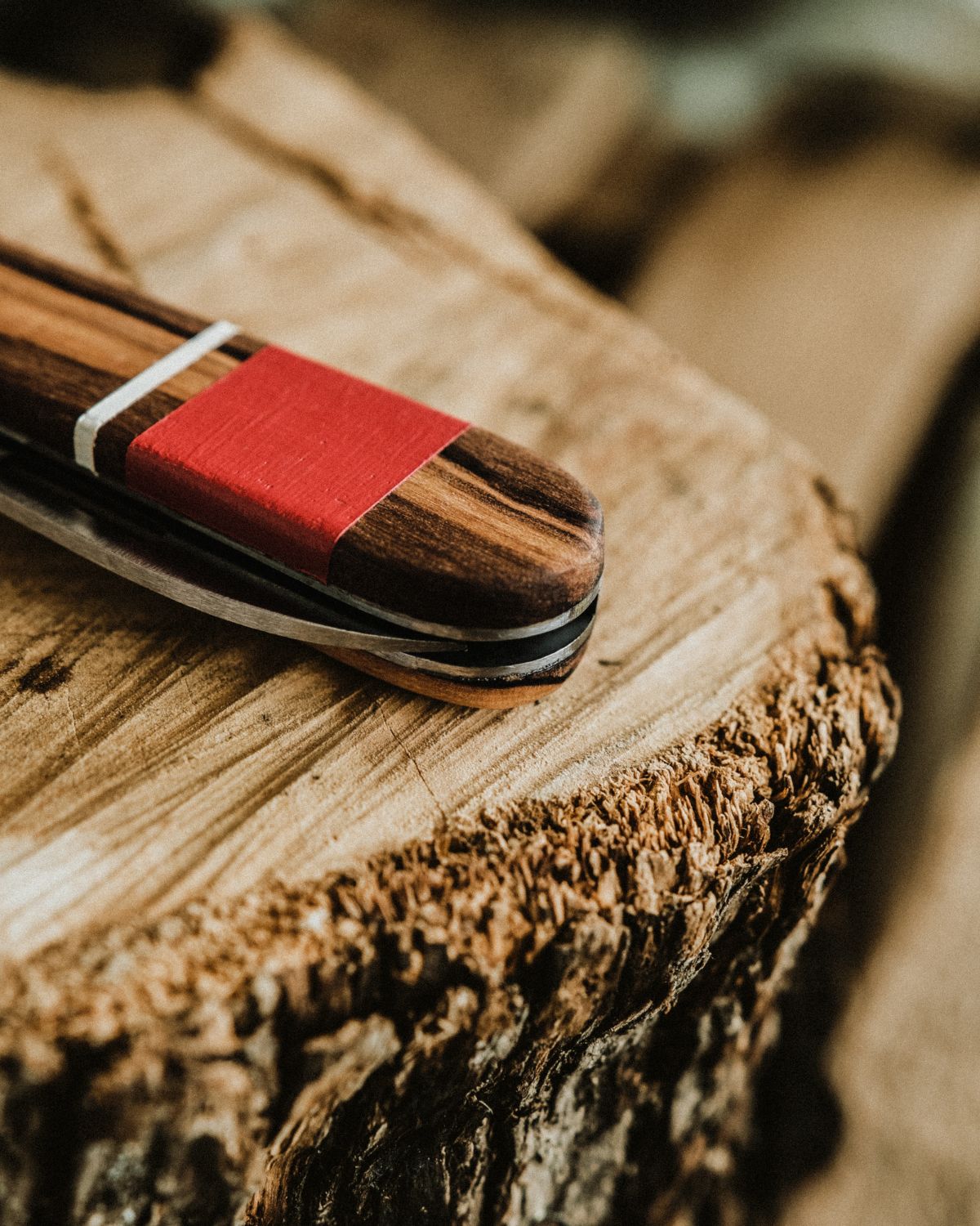 Close-up detail of a LOBO artisanal knife, showcasing the olive wood grain, a decorative red band, and the handcrafted bolster finish.