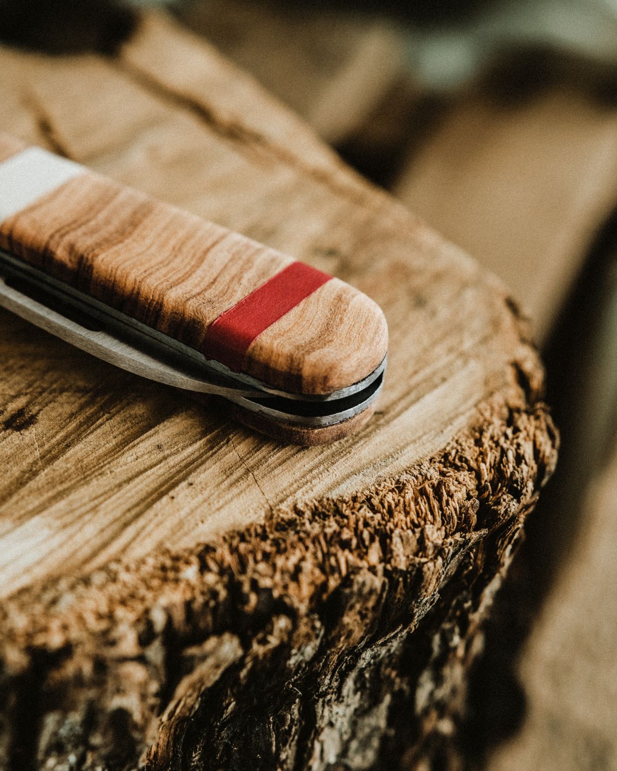 Detail of a LOBO artisanal knife by Fernando Mendes, focusing on the light olive wood handle with a decorative red band, resting on a rustic wood surface.