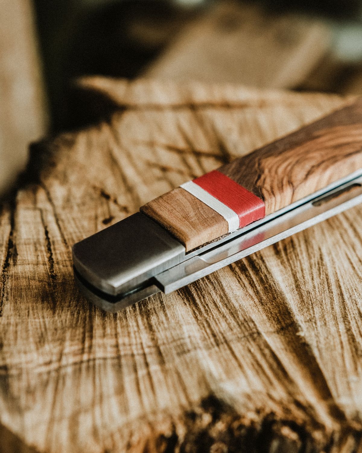 Macro shot of a LOBO knife handle, showcasing the natural olive wood texture and the decorative red and white band. Rustic yet contemporary design.